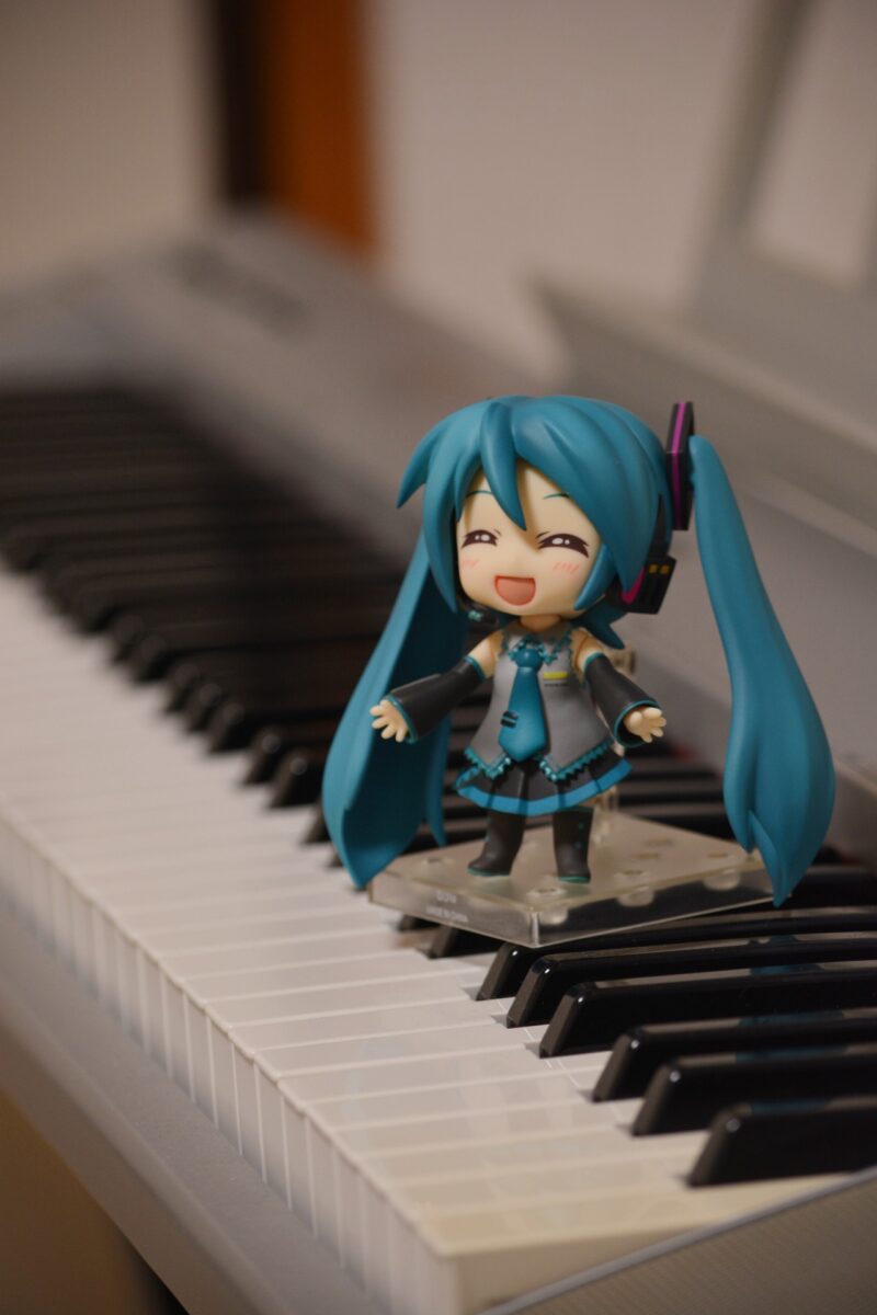 ピアノの上で両手を広げて満面の笑顔の初音ミク